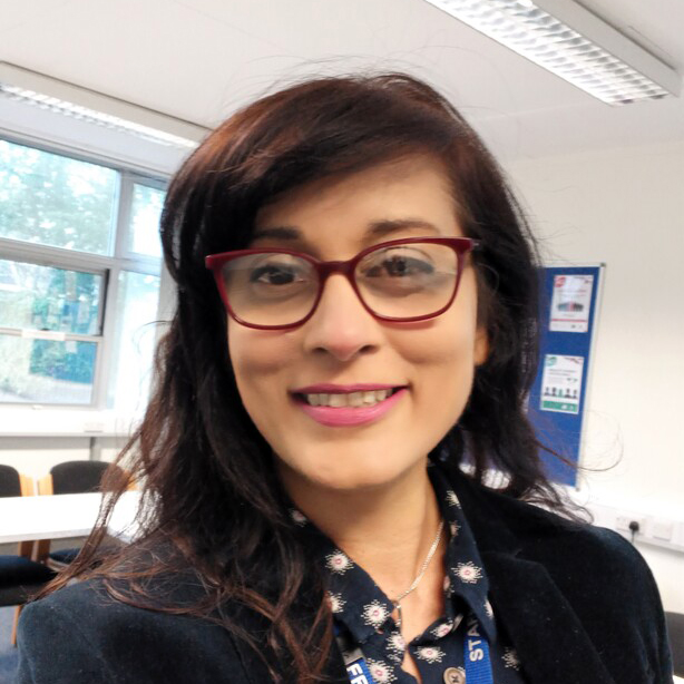 A photo of Carol Samlal, smiling at the camera with a classroom in the background